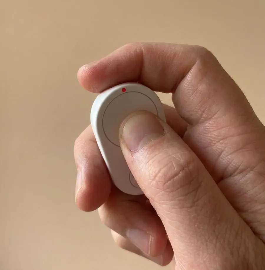 Thumb pushing the big button on a white Flic Cue
