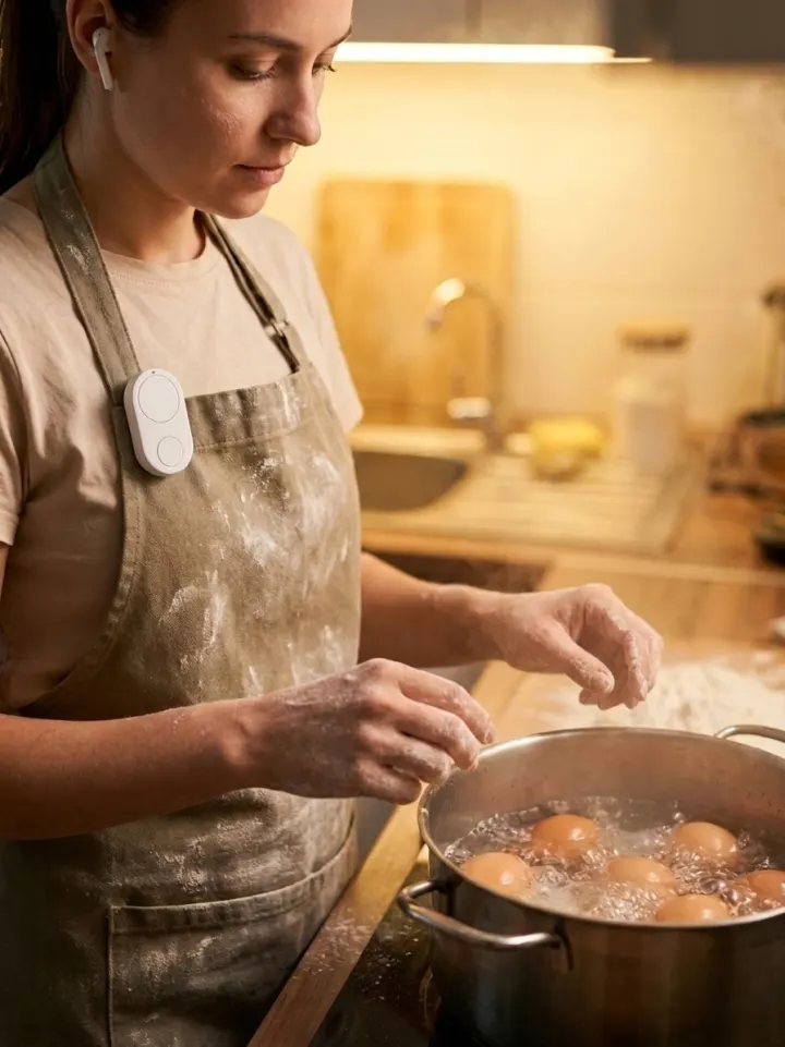 Woman boiling eggs, white Flic Cue clipped to her apron